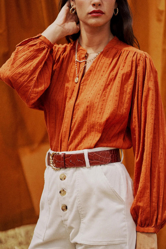 Model wearing a burnt orange blouse with embroidery detail