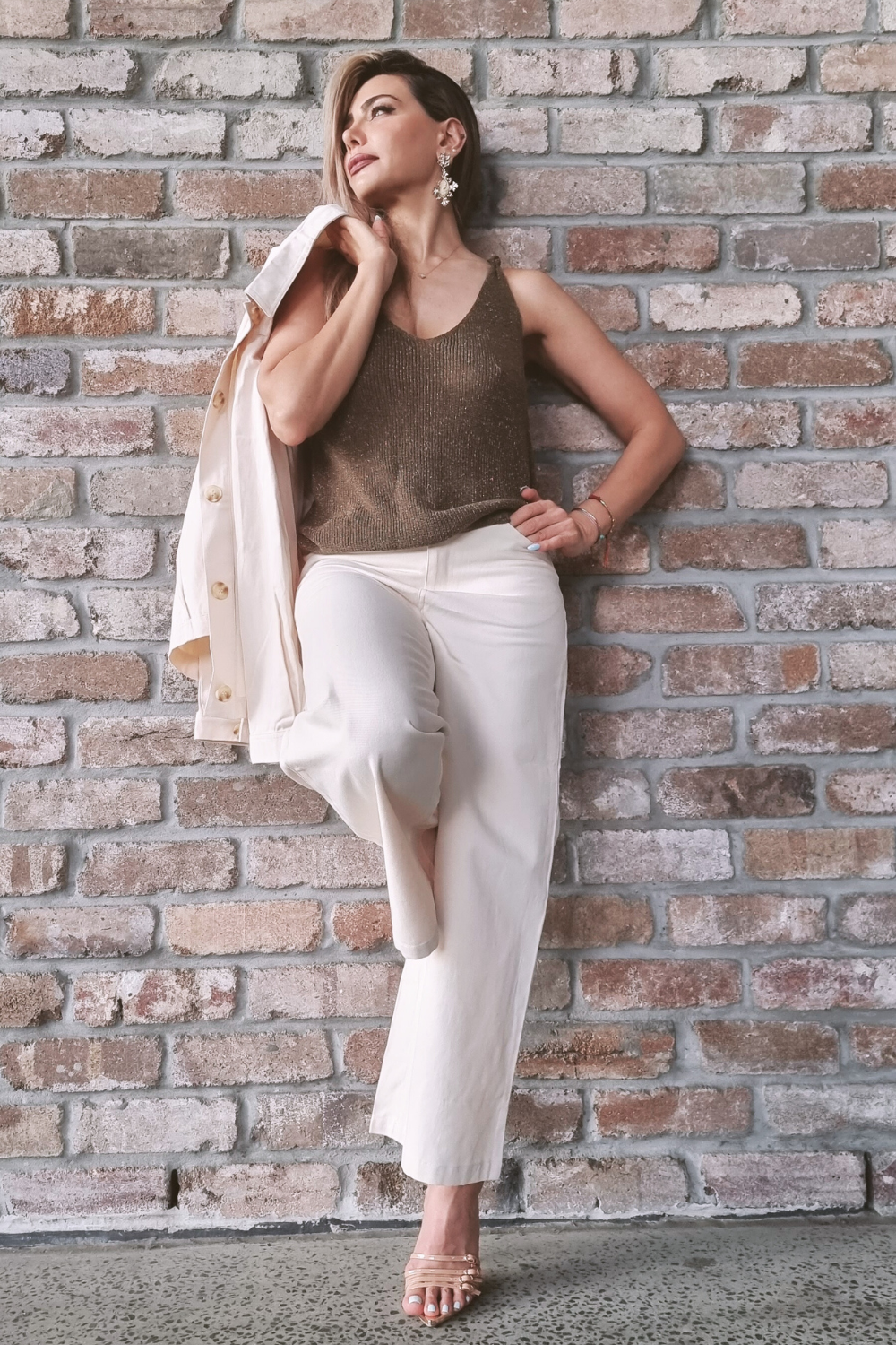 Woman standing against a wall wearing cream coloured wide leg pants