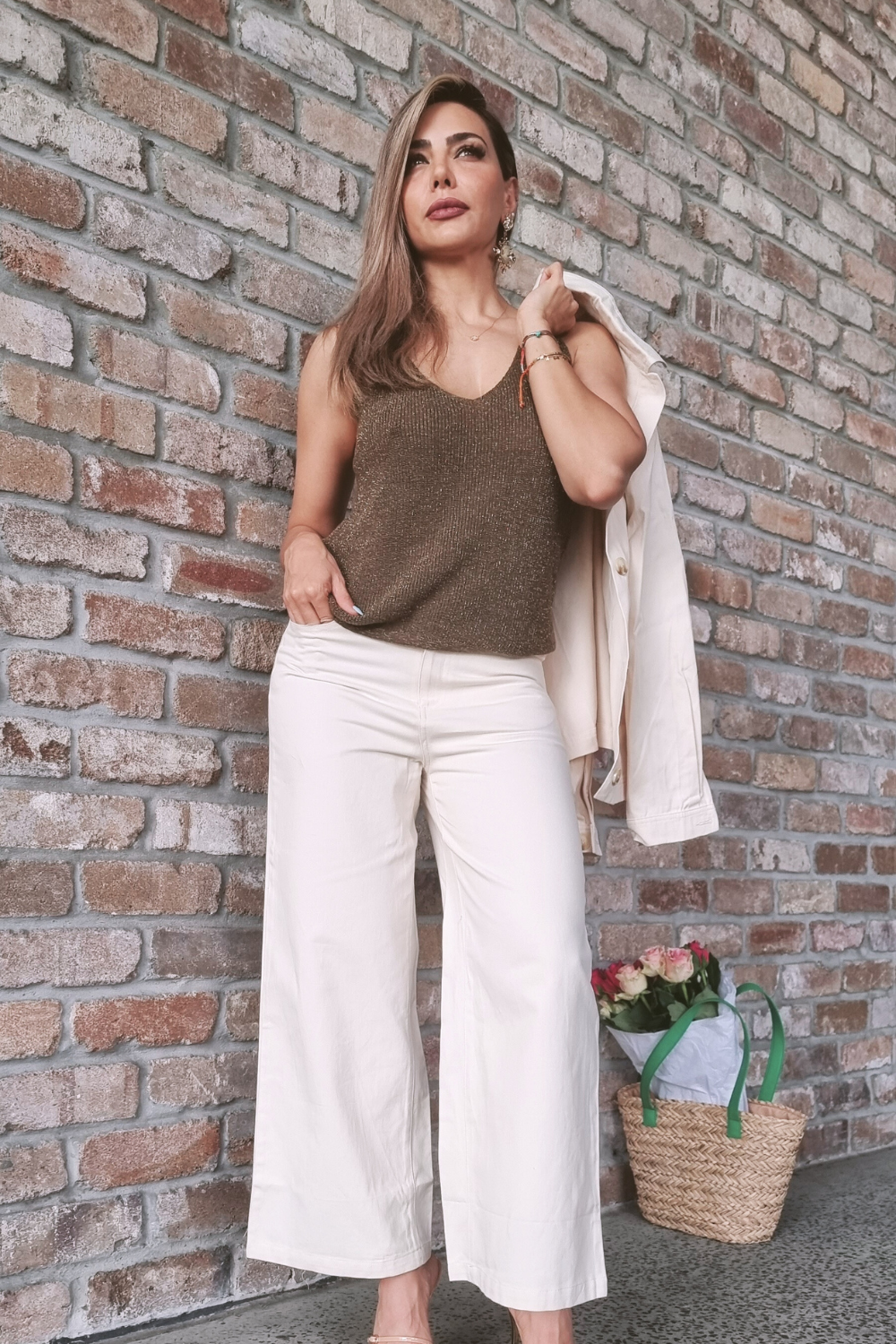 Woman standing against a wall wearing cream coloured wide leg pants