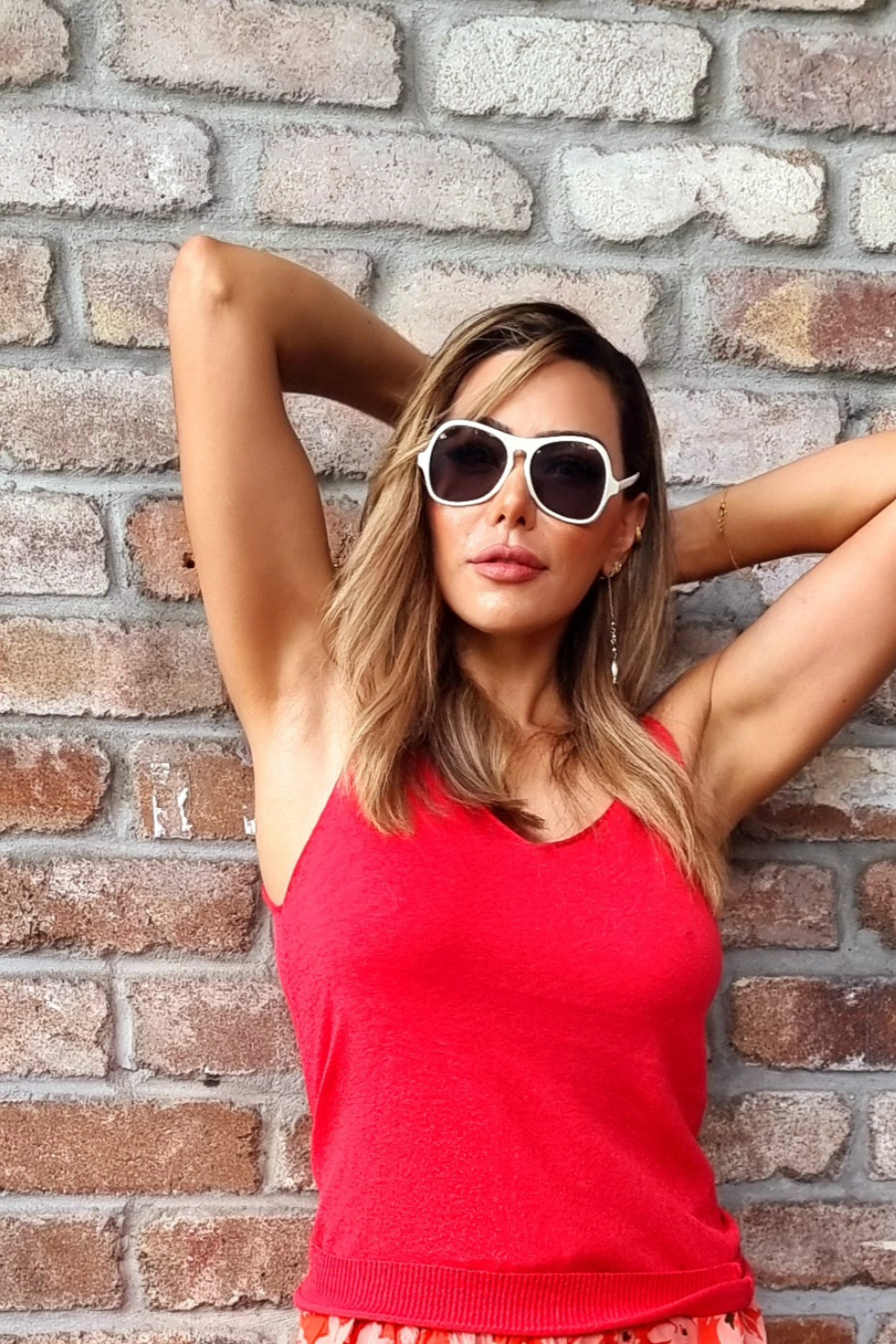 Woman standing against a wall wearing a coral red tank top