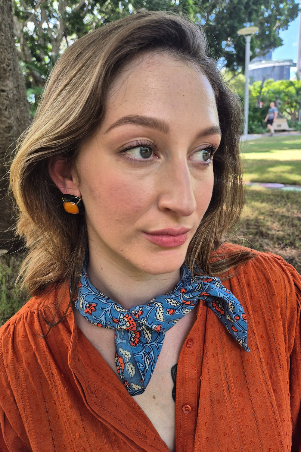 Woman wearing a blue neck scarf and burnt orange blouse