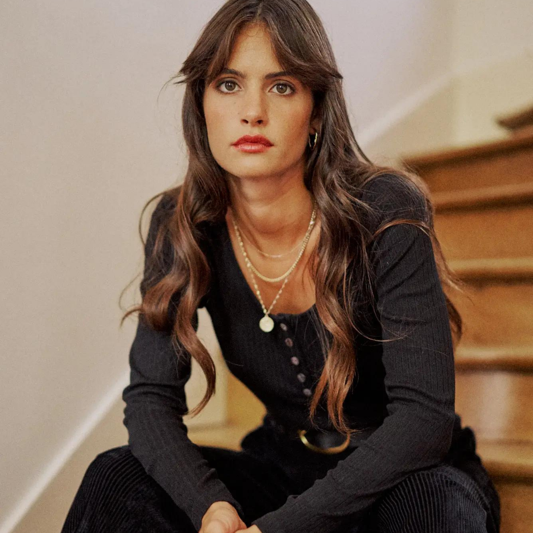 Model with long wavy hair wearing black velvet pants and black top