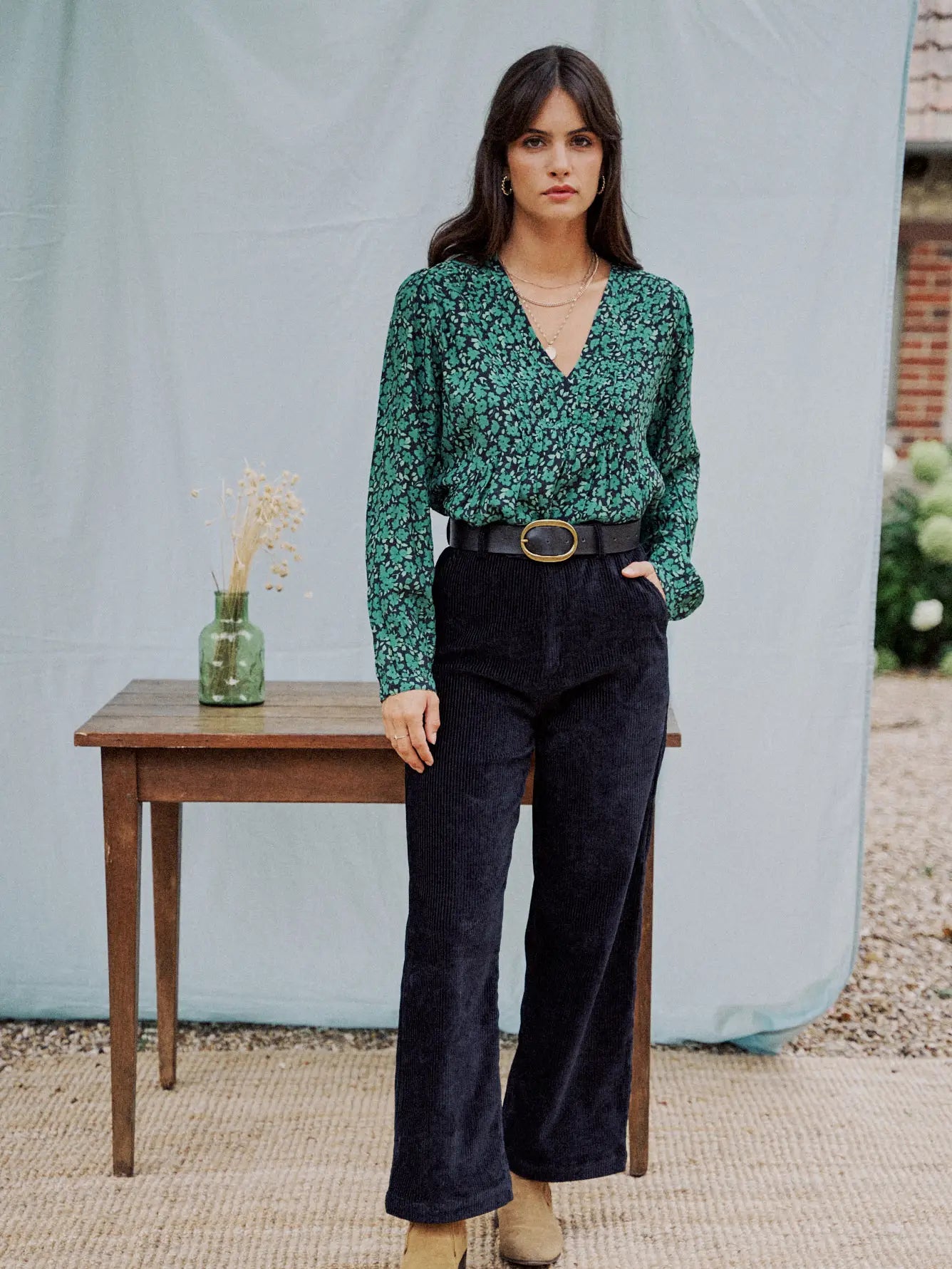 Woman modeling black velvet pants and green flower print blouse.